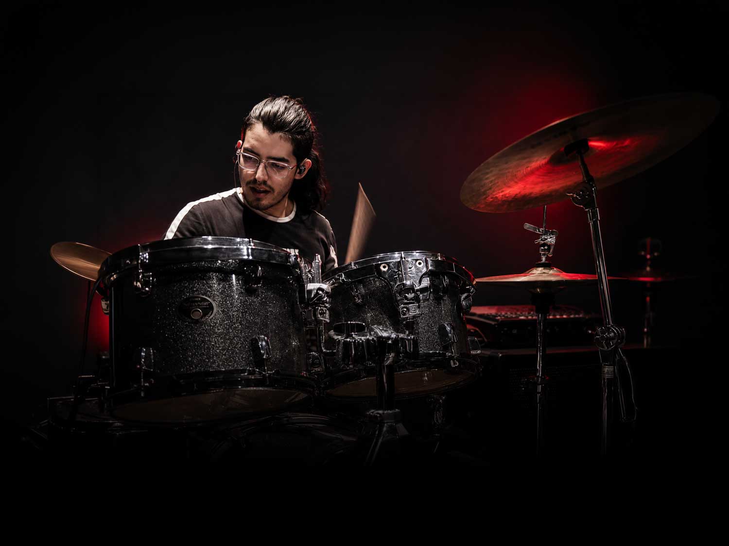 Baterista tocando un kit de batería bajo iluminación roja